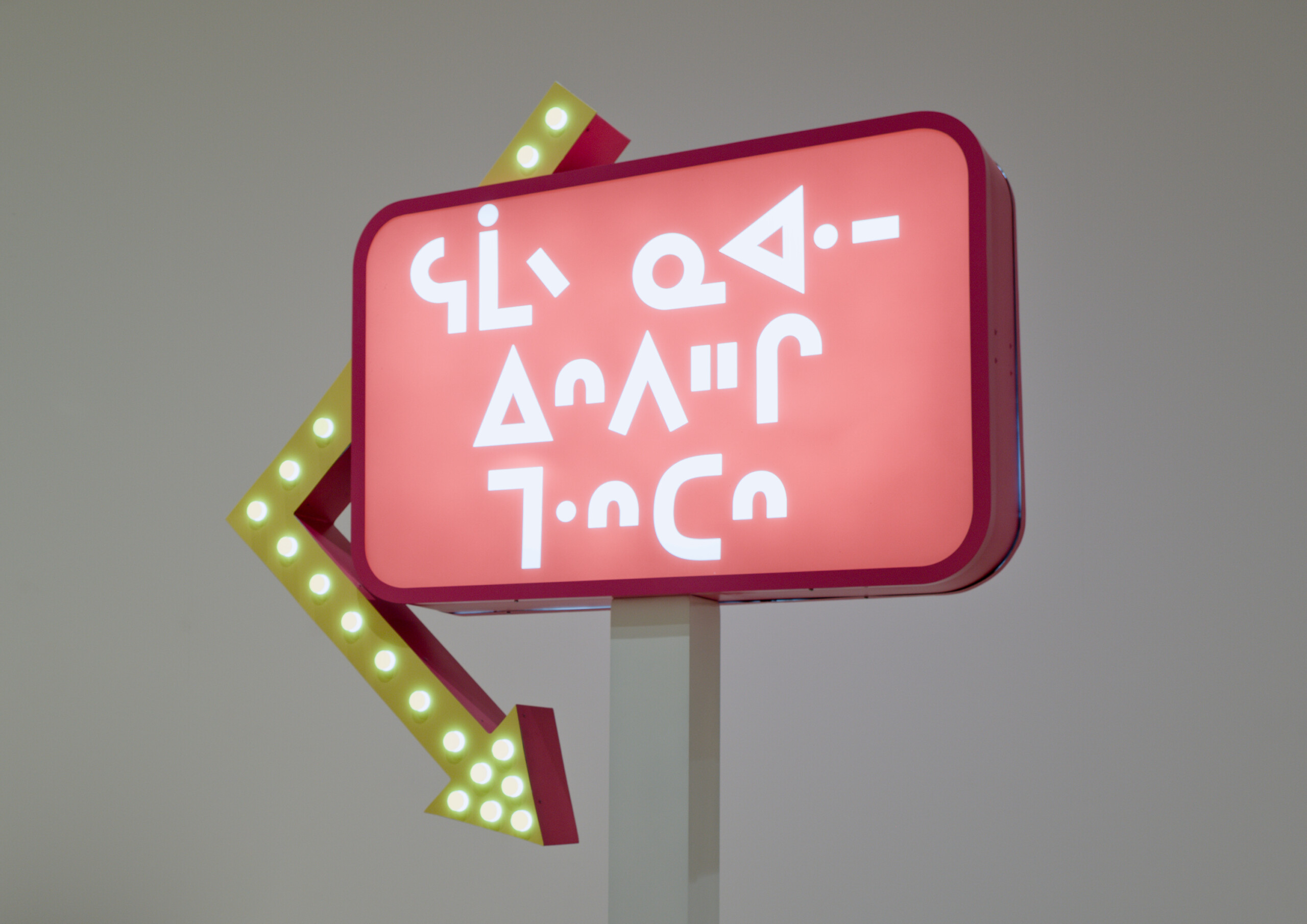 A neon sign in Cree with arrow pointing down.